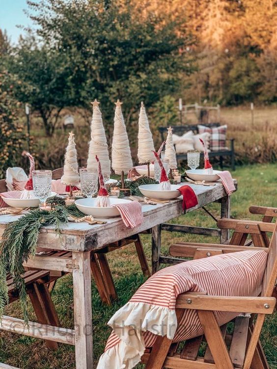 a creative outdoor Christmas tablescape with an evergreen runner, red and striped napkins, cone-shaped trees and gnomes in plates