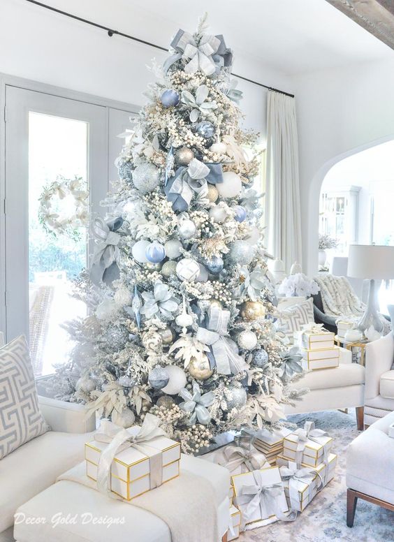 a delicate pastel blue Christmas tree with oversized pastel blue ornaments of various shades, gold ones and fabric blooms