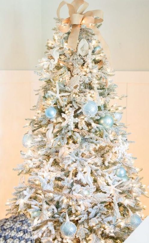 a dreamy coastal Christmas tree with light blue and mint buoy ornaments, sea horses, starfish, lights and a burlap bow on top