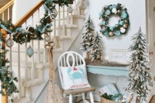a fantastic beach Christmas nook with an evergreen wreath with ribbons and metallic ornaments and a matching garland on the railing, flocked Christmas trees and a candle lantern with ornaments