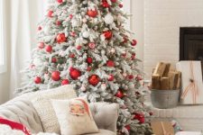 a flocked Christmas tree with red and white ornaments, a printed pillow and a white chunky knit blanket for a cozy feel