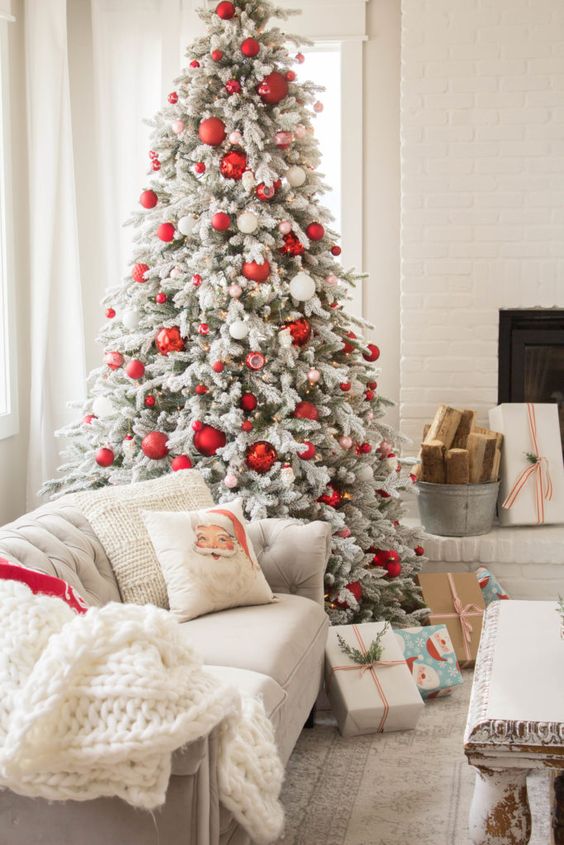 a flocked Christmas tree with red and white ornaments, a printed pillow and a white chunky knit blanket for a cozy feel