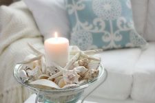 a glass bowl on a stand with seashells and starfish plus a pillar candle is a gorgeous beach Christmas decoration