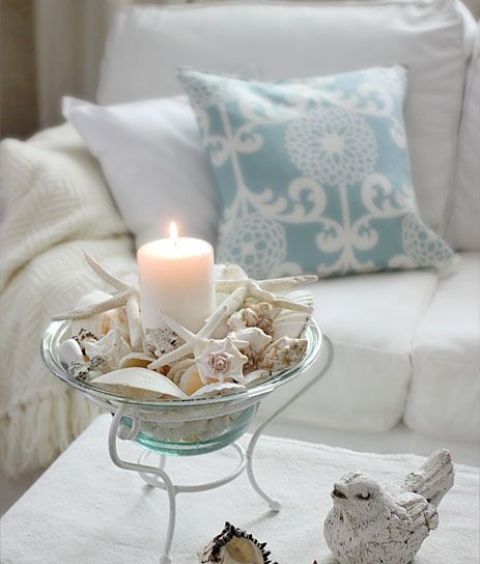 a glass bowl on a stand with seashells and starfish plus a pillar candle is a gorgeous beach Christmas decoration