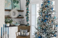 a gorgeous coastal Christmas space with an evergreen and turquoise ornament garland, a flocked Christmas tree with light blue and electric blue ornaments