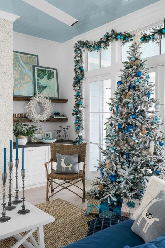 a gorgeous coastal Christmas space with an evergreen and turquoise ornament garland, a flocked Christmas tree with light blue and electric blue ornaments