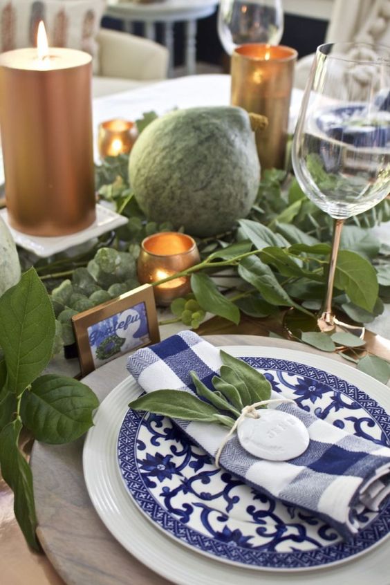 a greenery and copper tablescape with blue and white plates and napkins plus cards make up a gorgeous setting for Thanksgiving
