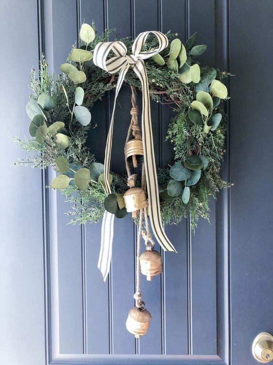 a greenery and foliage Christmas wreath with a striped bow and large vintage bells is a lovely and chic decoration