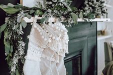 a greenery garland with flocked mini trees and white boho sotckings with fringe for elegant natural decor