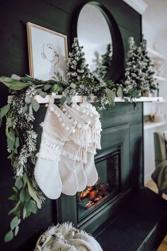 a greenery garland with flocked mini trees and white boho sotckings with fringe for elegant natural decor