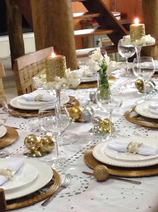 a holiday tablescape with gold and silver ornaments, wicker chargers, glitter candles and white blooms