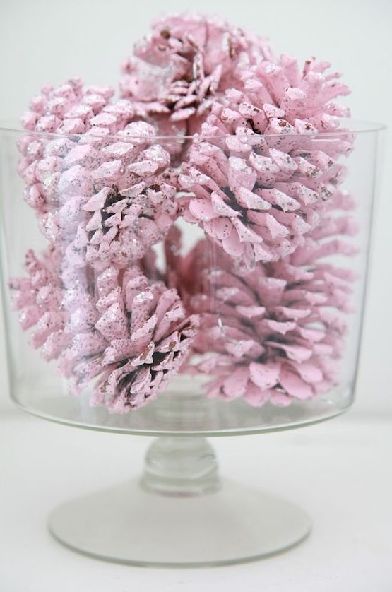 a large glass bowl with pastel pink pinecones is a pretty modern decoration for the holidays and it will add a soft touch to the spac