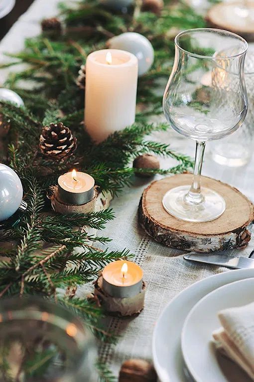 a lovely outdoor Christmas tablescape with neutral linens, an evergreen table runner, snowy pinecones, nuts and candles