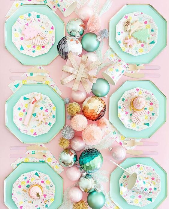 a lovely pastel Christmas tablescape with a pink tablecloth, mint grene hex plates, a pastel ornament garland and bright plates