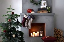 a mini Christmas tree with bright ornaments, stacked pillows, bright stockings, a flocked greenery wreath and firewood