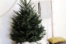 a mini Christmas tree with lights in a basket with white faux fur is a stylish and minimal idea
