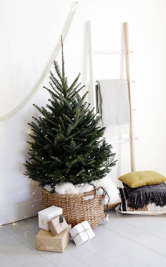 a mini Christmas tree with lights in a basket with white faux fur is a stylish and minimal idea