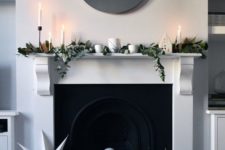 a minimalist Christmas mantel decorated with magnolia leaves and eucalyptus plus white candles and black and white stars