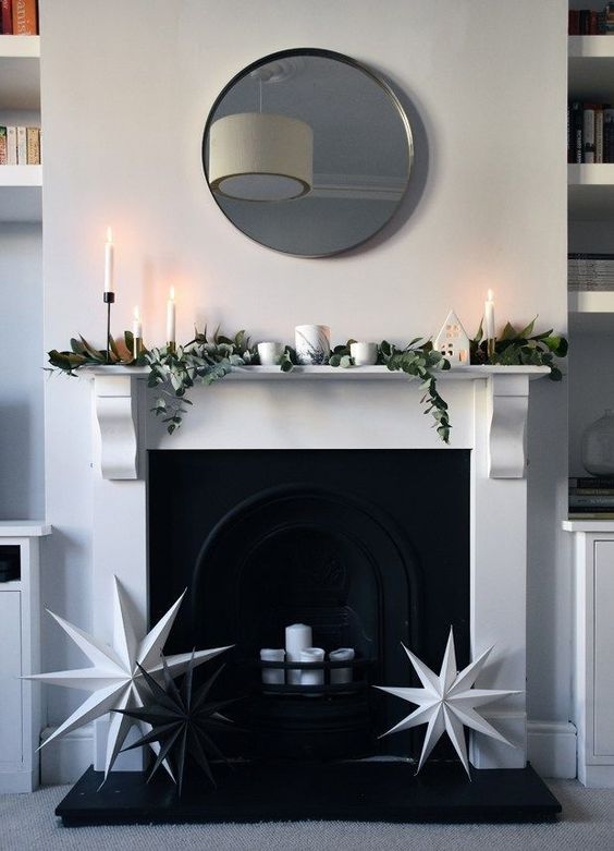 a minimalist Christmas mantel decorated with magnolia leaves and eucalyptus plus white candles and black and white stars