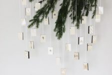 a minimalist advent calendar with evergreens and suspended boxes for each day looks rustic and minimal
