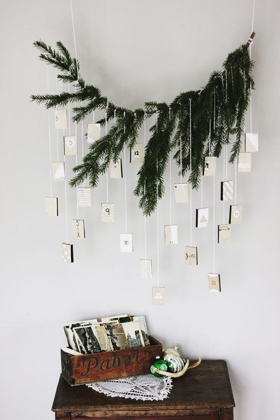 a minimalist advent calendar with evergreens and suspended boxes for each day looks rustic and minimal