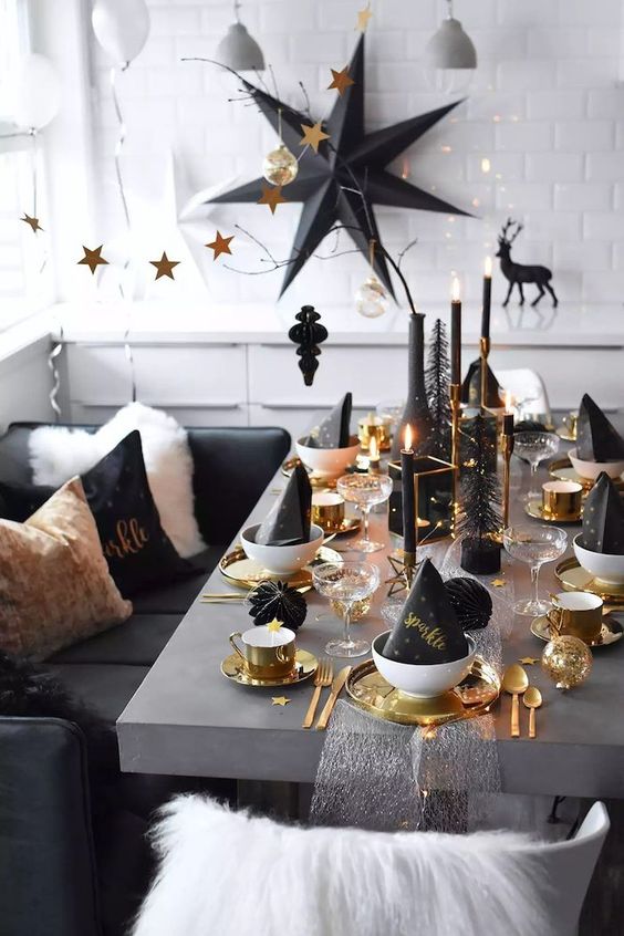 a modern NYE tablescape with black cone hats, gold chargers and mugs, black candles in gold candleholders and black bottle brush trees