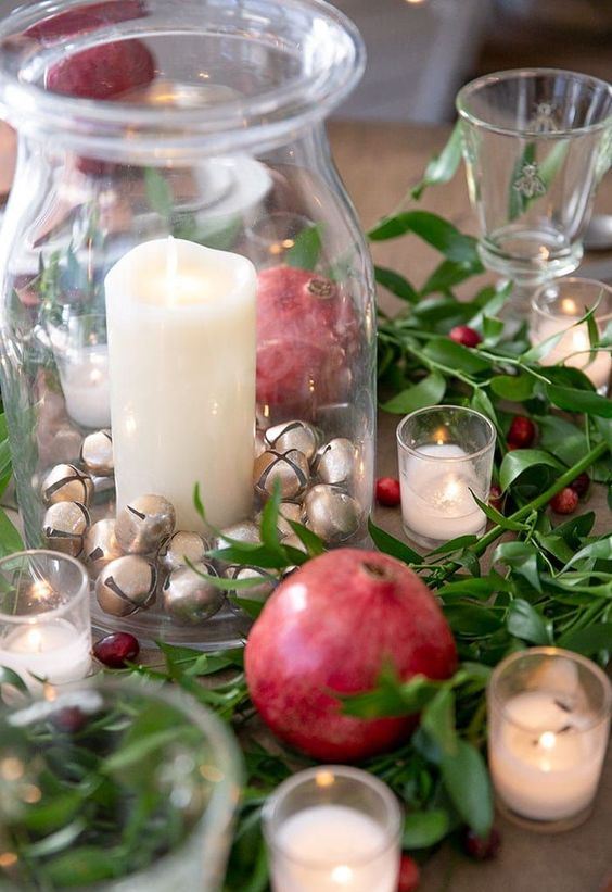a natural Christmas centerpiece of greenery, berries, pomegranates, candles and a glass jar with mini bells and candles