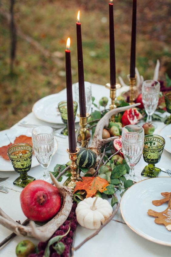 a natural Thanksgiving table runner of greenery, antlers, pumpkins and pomegranates plsu burgundy candles