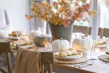 a natural Thanksgiving tablescape with neutral pumpkins, fall leaves, candles and woven chargers is a lovely idea