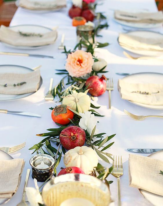 a pretty Thanksgiving table runner with pomegranates, white pumpkins, blush blooms and greenery plus candles