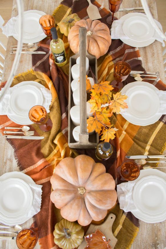 a pretty natural Thanksgiving tablescape with whitewashed pumpkins, fall leaves, a plaid tablecloth and amber glasses