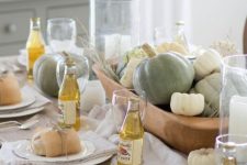 a pretty neutral Thanksgiving tablescape with a bowl filled with pumpkins and more pumpkins around looks chic