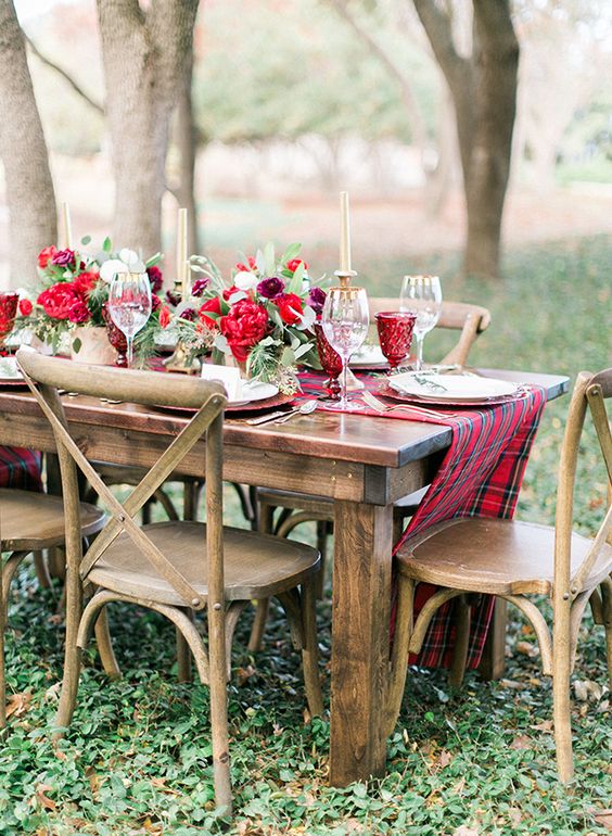 a refined Christmas tablescape with a plaid table runner, bold red blooms and red glasses, tall and thin candles and white porcelain