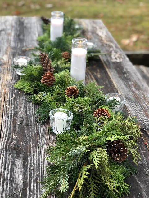 a rustic Christmas tablescape with an uncovered table, an evergreen runner with candles and pinecones is a cozy idea