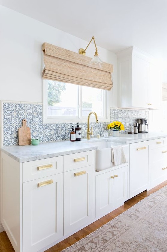 a serene white farmhouse kitchen with shaker cabinets, with white marble countertops and blue Moroccan tiles on the backsplash