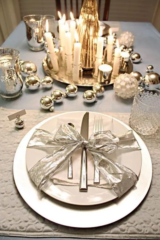 a shiny table setting with silver ornaments, mercury glass candle holders and candles