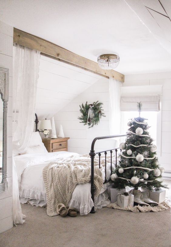 a small Christmas tree with white and silver ornaments, gift boxes and an evergreen wreath with pinecones for holiday decor