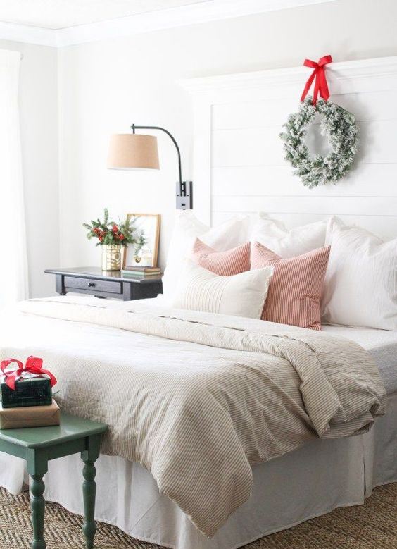 a snowy evergreen wreath with a red bow, greenery and berries in a metallic vase, some gift boxes on the bench