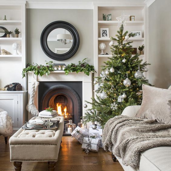 a stylish Christmas tree with silver ornaments, a stocking and a greeneyr garland with pinecones on the mantel