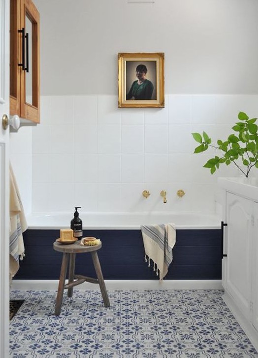a stylish modern bathroom with blue Moroccan tiles, a bathtub clad with navy tiles, a cabinet, an artwork and a white vanity