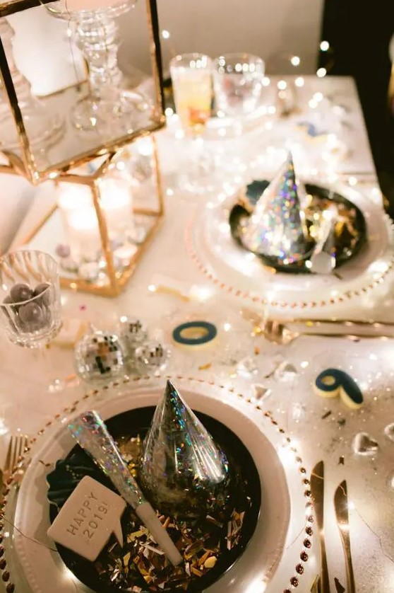 a super shiny NYE party tablescape in gold and white, with stacked candleholders, white plates and clear chargers, gold cutlery and disco balls