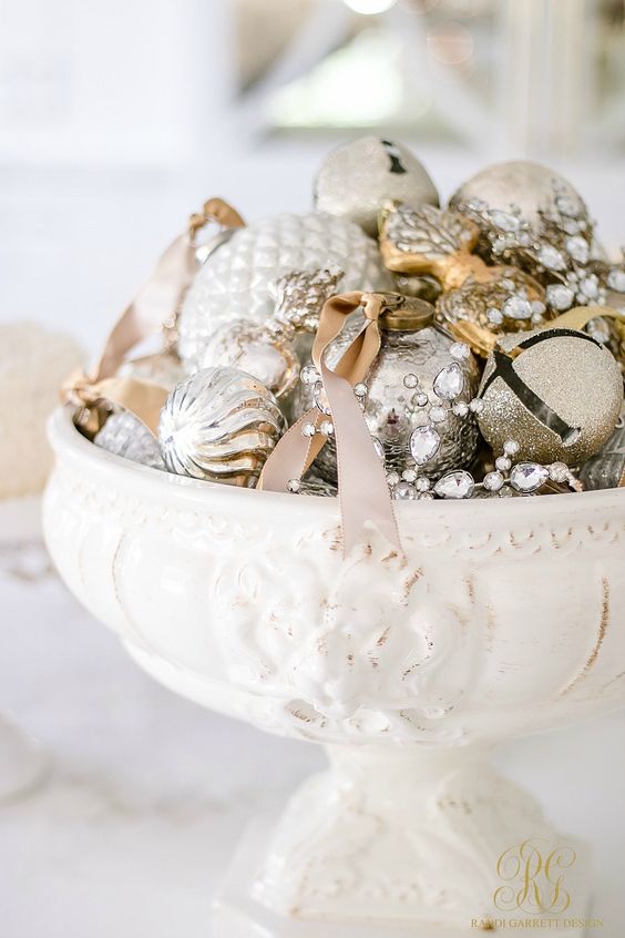 a vintage white bowl with silver and gold glitter Christmas ornaments and bells plus crystals and ribbons as a refined holiday centerpiece
