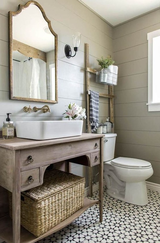 a welcoming farmhouse bathroom with grey planked walls, a Moroccan tile floor, a wooden vanity, a mirror in a wooden frame