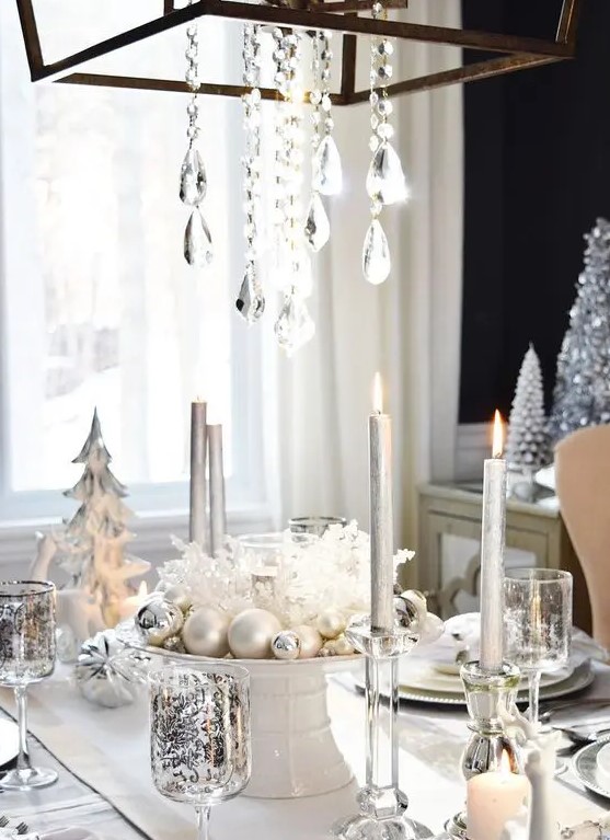 a white and silver table setting with pearly and silver ornaments, a crystal chandelier and patterned glasses