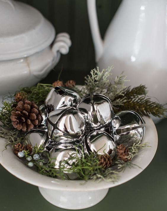 a white bowl with grass, berries, pinecones and silver bells is a chic and cozy natural Christmas decoration to rock