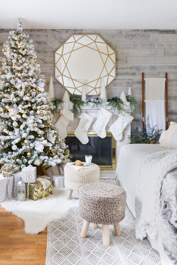 a winter wonderland living room with a flocked Christmas tree with white and gold ornaments, white stockings, mini Christmas trees and fir branches