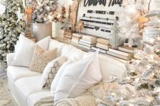 a winter wonderland living room with several flocked Christmas trees with lights, some more mini trees and lots of white paper snowflakes