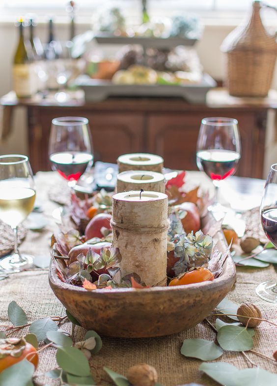 a wooden bowl with blooms, persimmons, pears and candles in wooden stumps plus nuts and leaves around