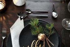 black plates, a neutral napkin, a gold bell with leather cords and fir twigs for a modern Christmas place setting