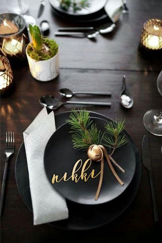 black plates, a neutral napkin, a gold bell with leather cords and fir twigs for a modern Christmas place setting